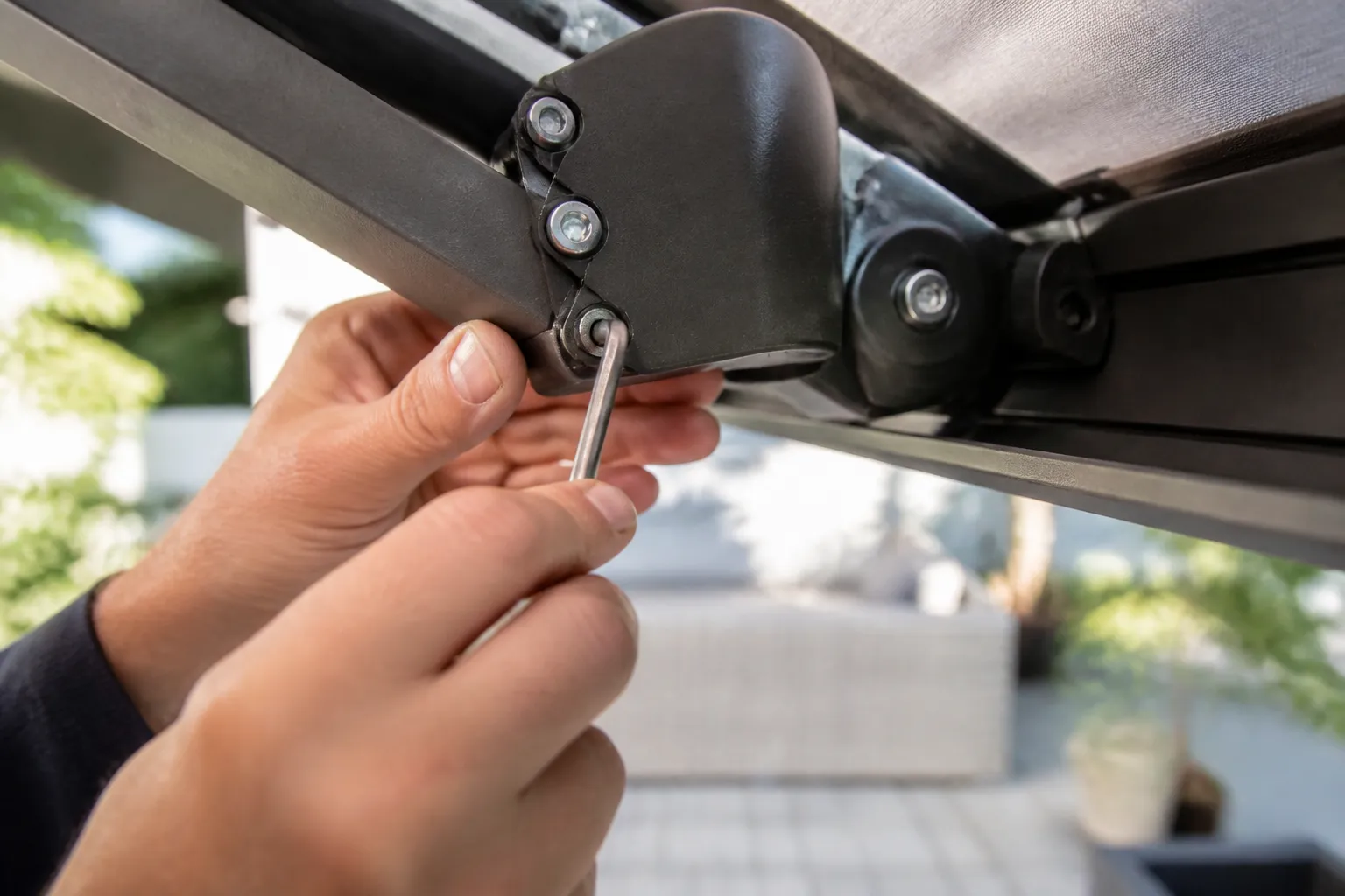 Mains ajustant le mécanisme d’un bras de store banne avec une clé