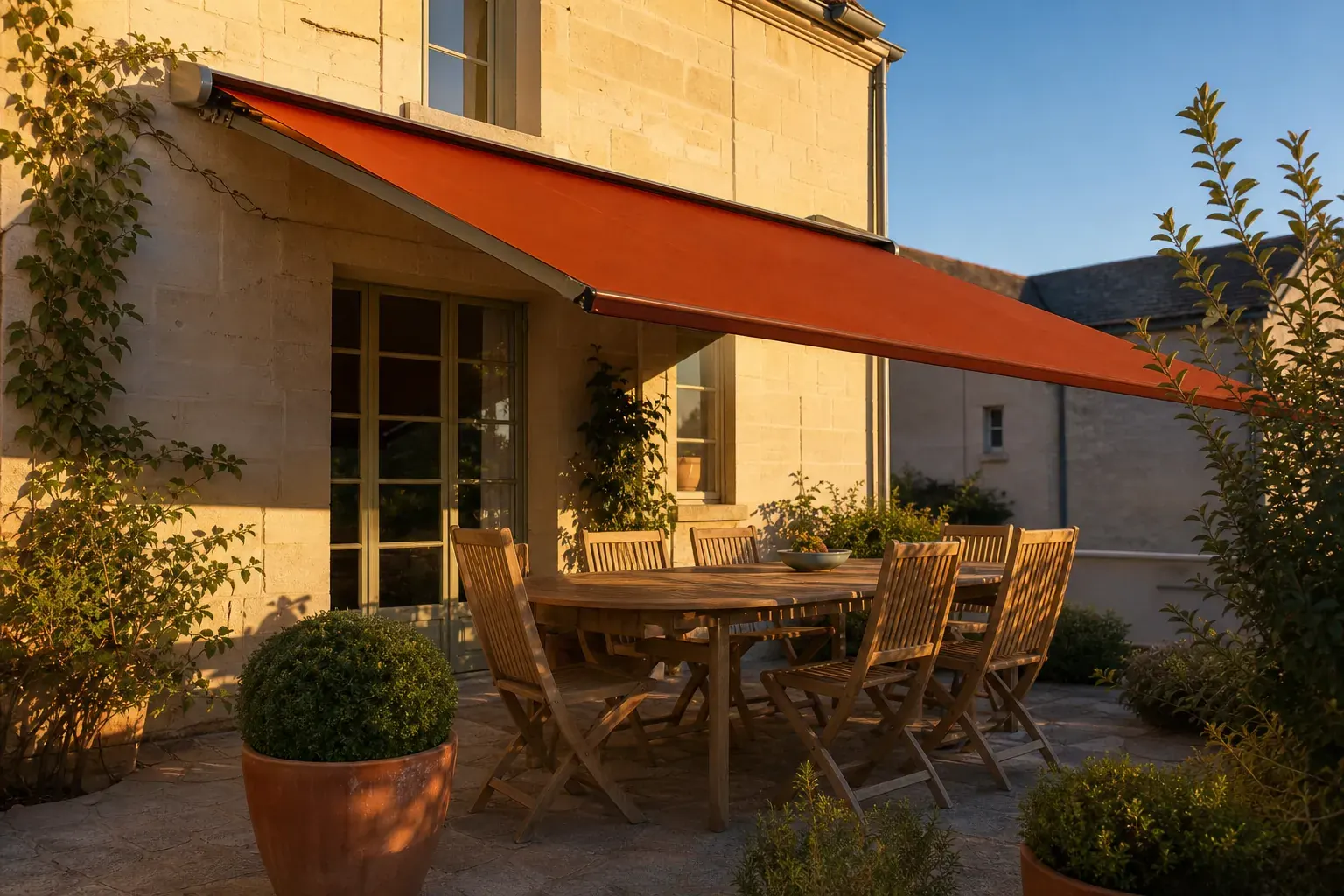 Terrasse angevine en fin d’après-midi sous un store banne terre cuite entièrement déployé