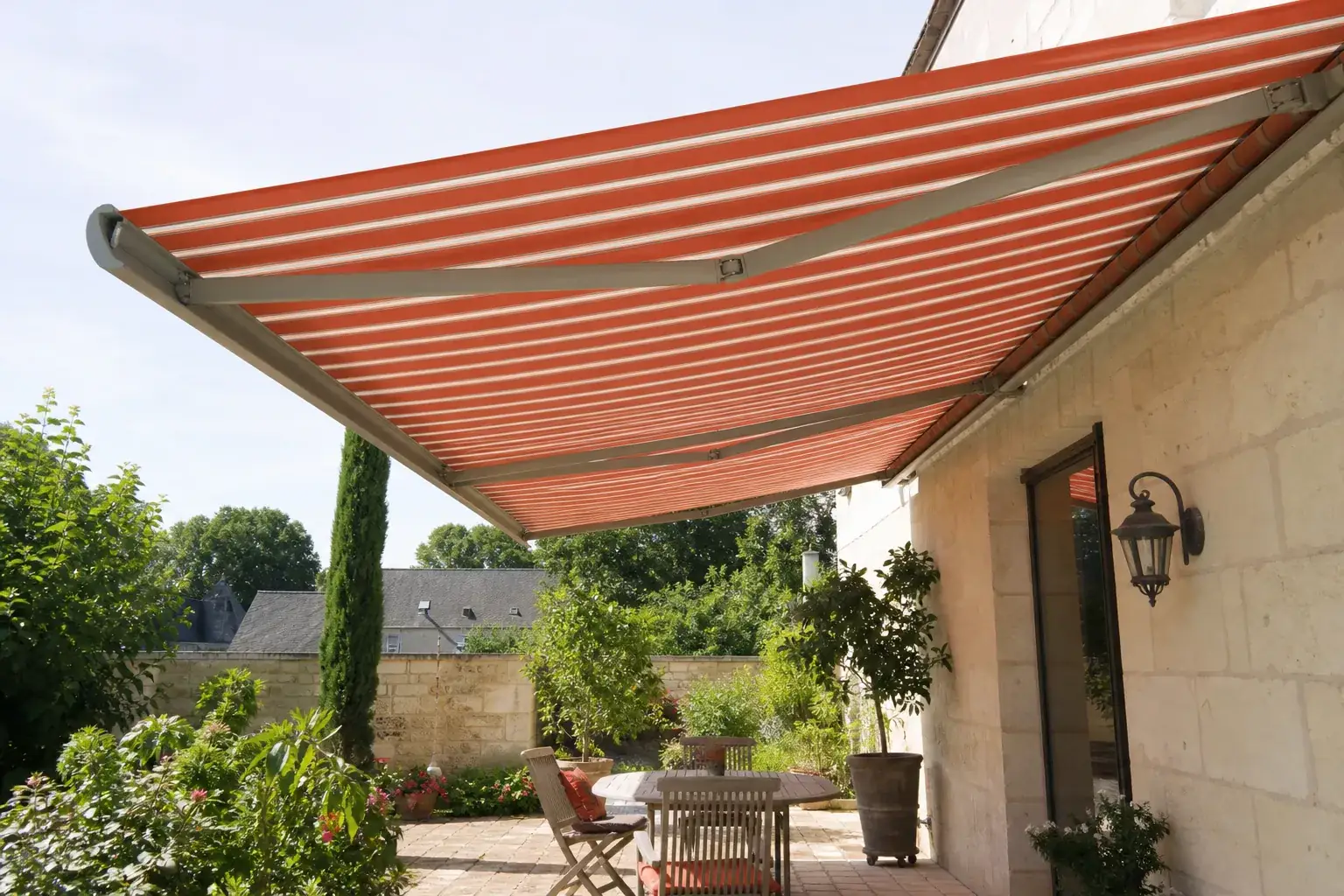 Store banne aluminium et toile terre cuite déployé sur une terrasse pavée devant une façade en tuffeau clair