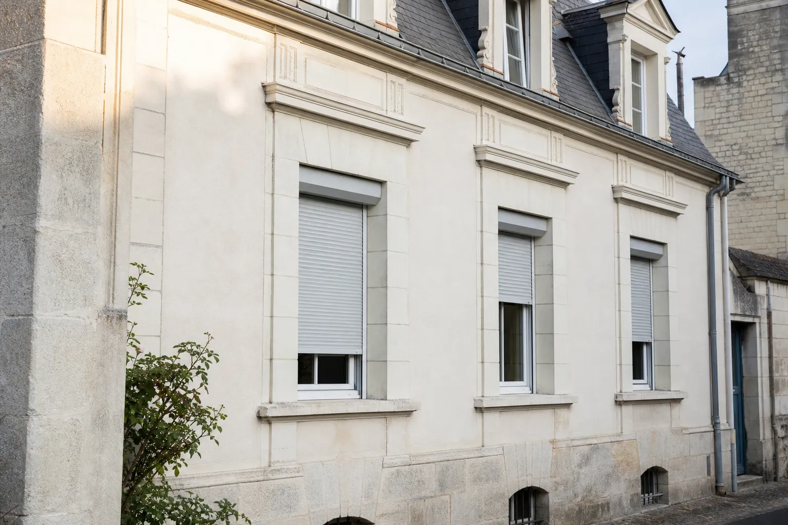 Façade avec fenêtres équipées de volets roulants aluminium gris clair, certains ouverts, lumière de matin